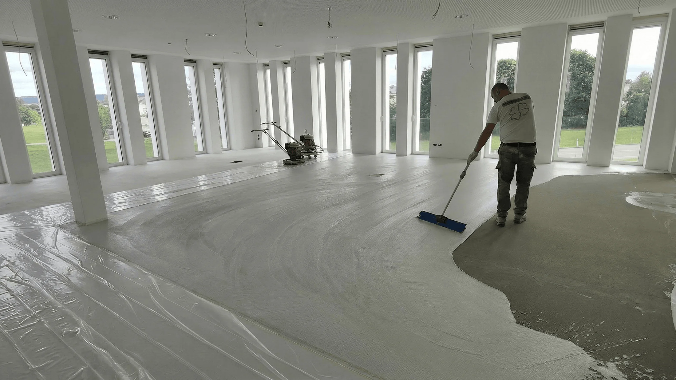 Applicazione di pavimento continuo in Architop bianco in un ampio spazio commerciale, operatore che stende il prodotto con spatola a manico lungo su fondo in calcestruzzo.