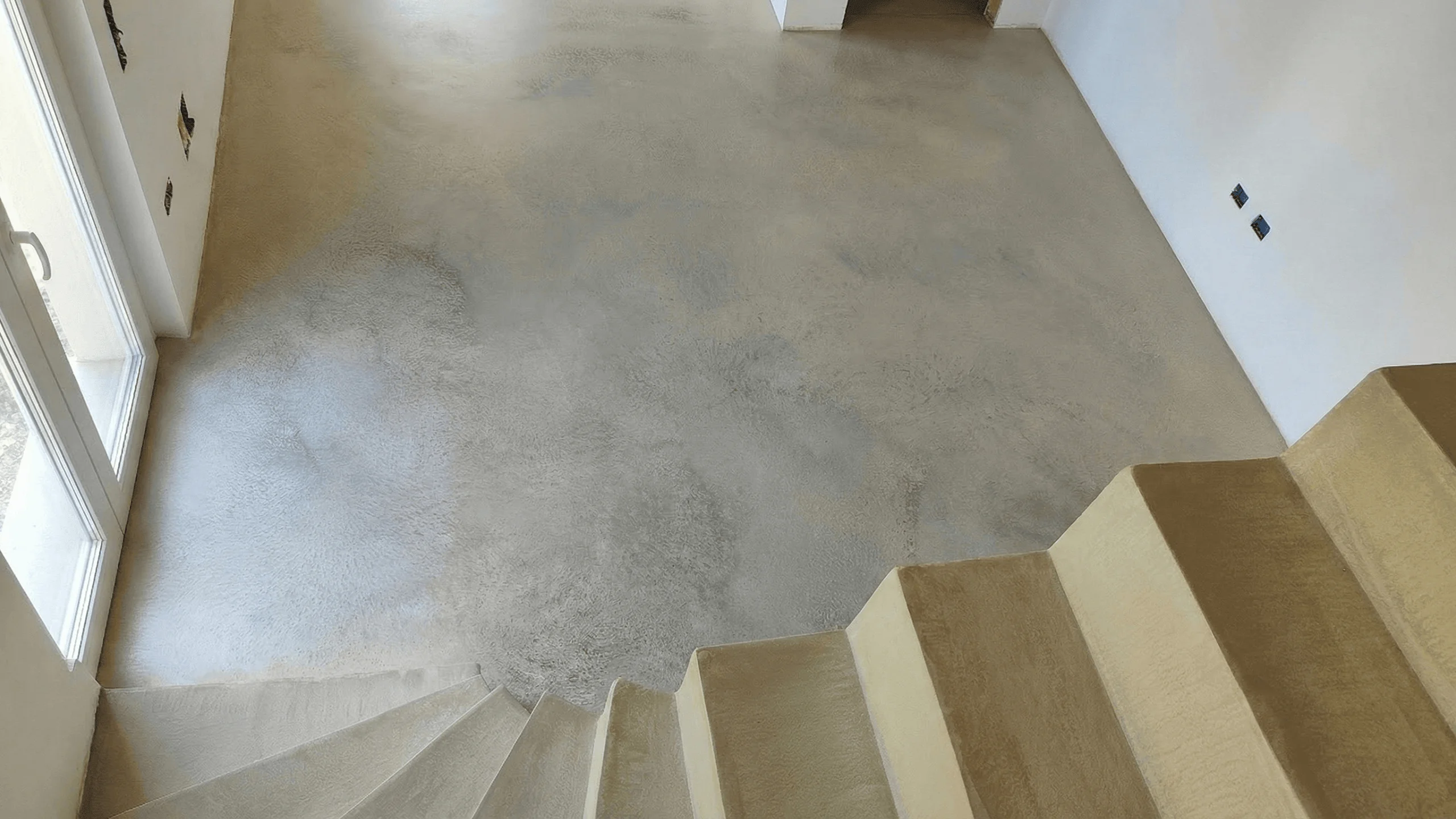 Scala interna che scende su pavimento continuo in Architop effetto nuvolato grigio-beige in abitazione moderna.