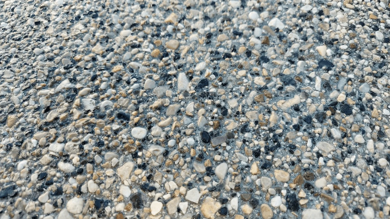 Dettaglio ravvicinato di pavimento esterno in ghiaino lavato con ciottoli a vista di diverse dimensioni e colori.