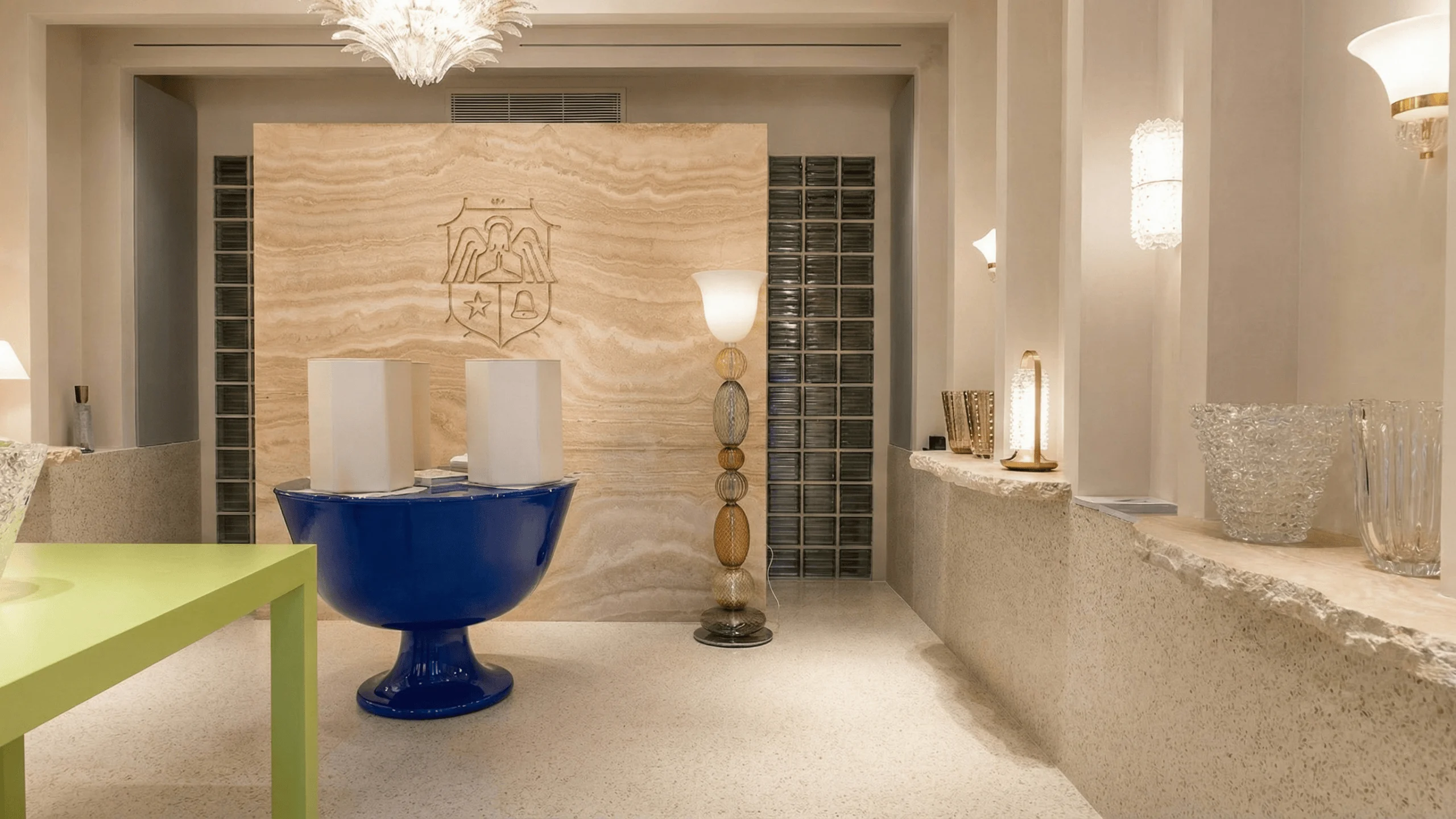 Interno elegante con pavimento continuo in Lixio chiaro effetto terrazzo, arredi di design e pareti illuminate da applique e lampade decorative.