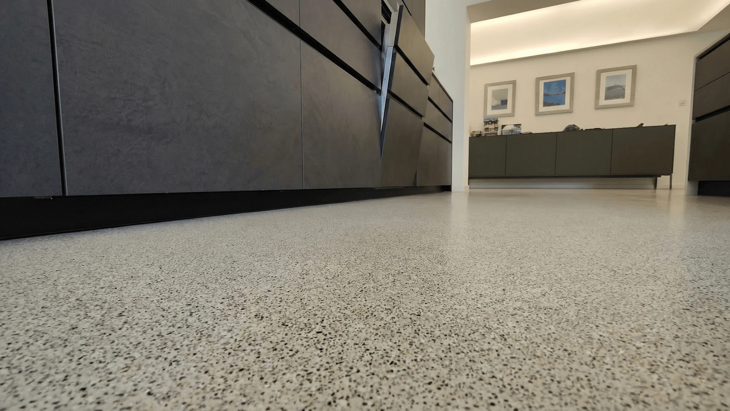 Dettaglio ravvicinato di pavimento continuo in Lixio chiaro effetto terrazzo in ambiente moderno con arredi scuri.