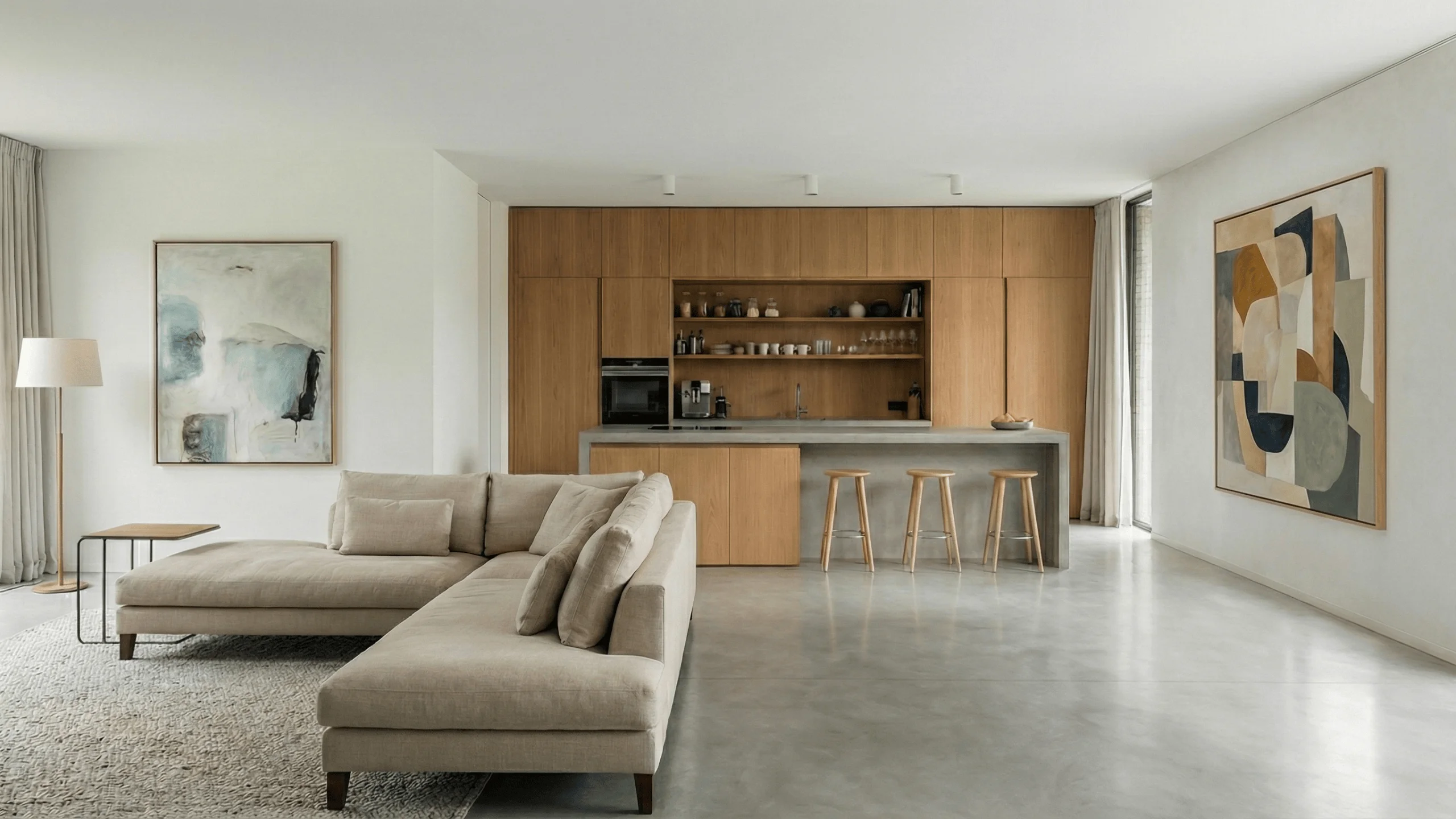Zona giorno open space con cucina in legno e grande divano beige su pavimento continuo in microcemento grigio chiaro effetto nuvolato.